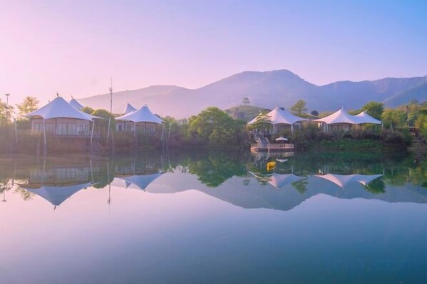 A tranquil lakeside setting with yurts and a boat, surrounded by mountains.
