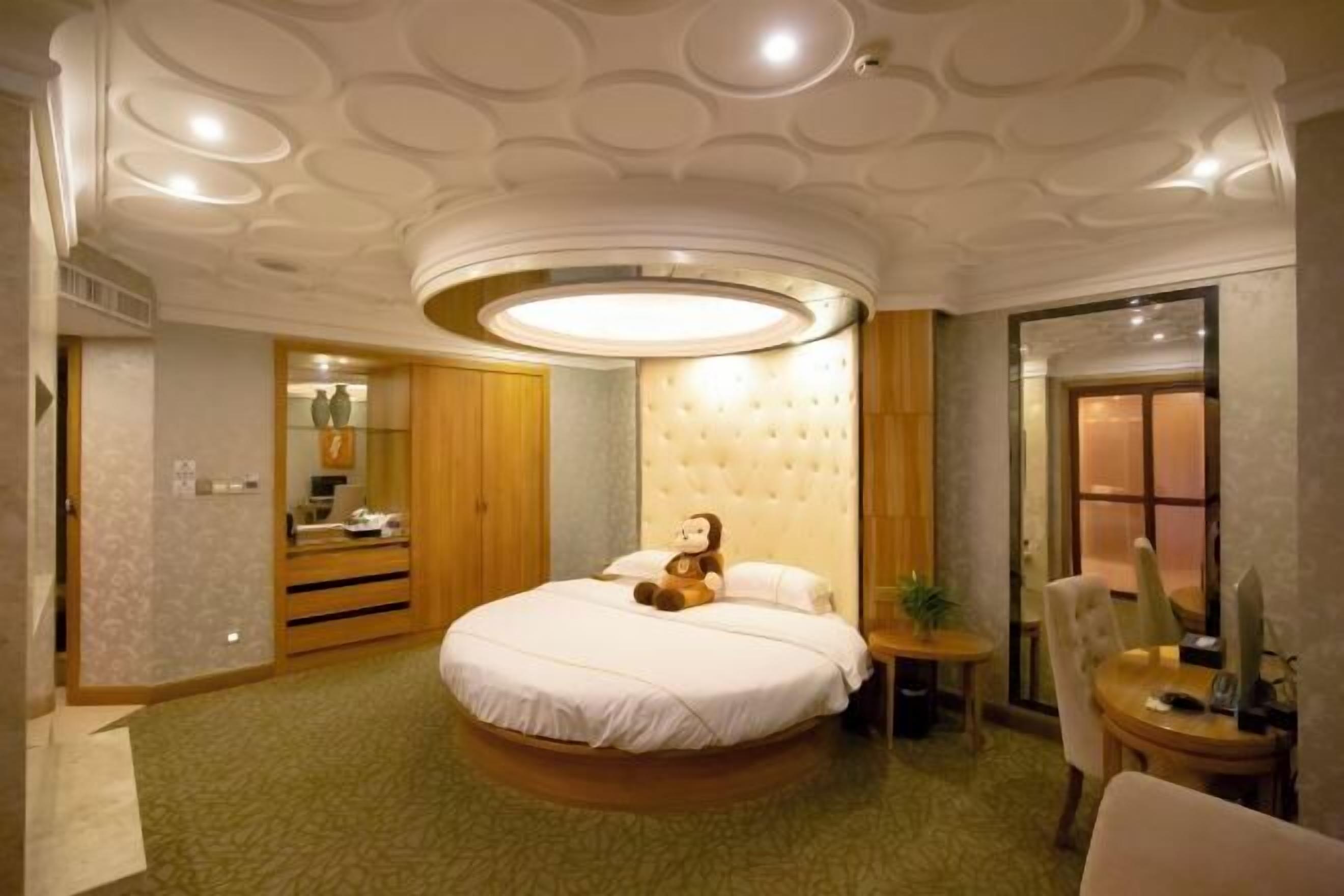 A bedroom with a round bed, a tufted headboard, a bedside table, and a chair.