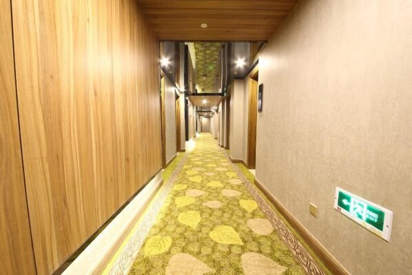 Un couloir d’hôtel avec des lambris en bois, une moquette à motifs et un panneau de sortie vert.