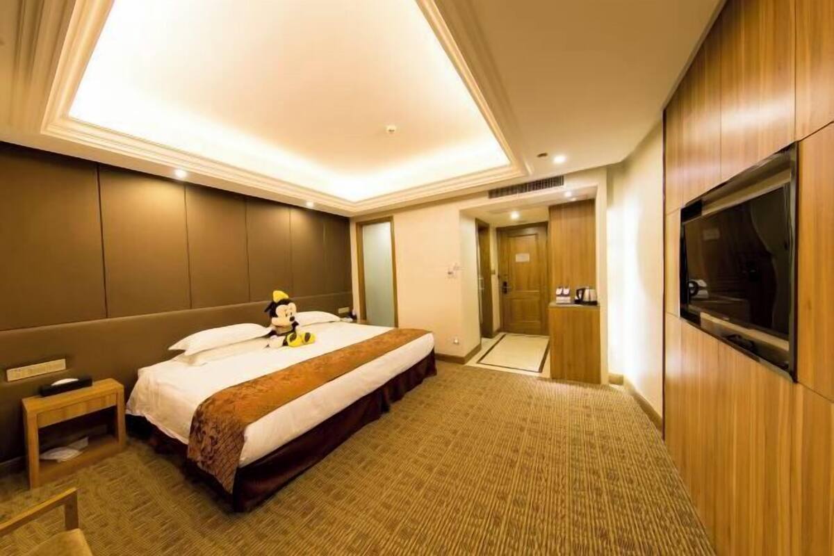 Ein Hotelzimmer mit einem Bett, einem kleinen Nachttisch, einem an der Wand befestigten Fernseher und einer Tür zum Badezimmer.