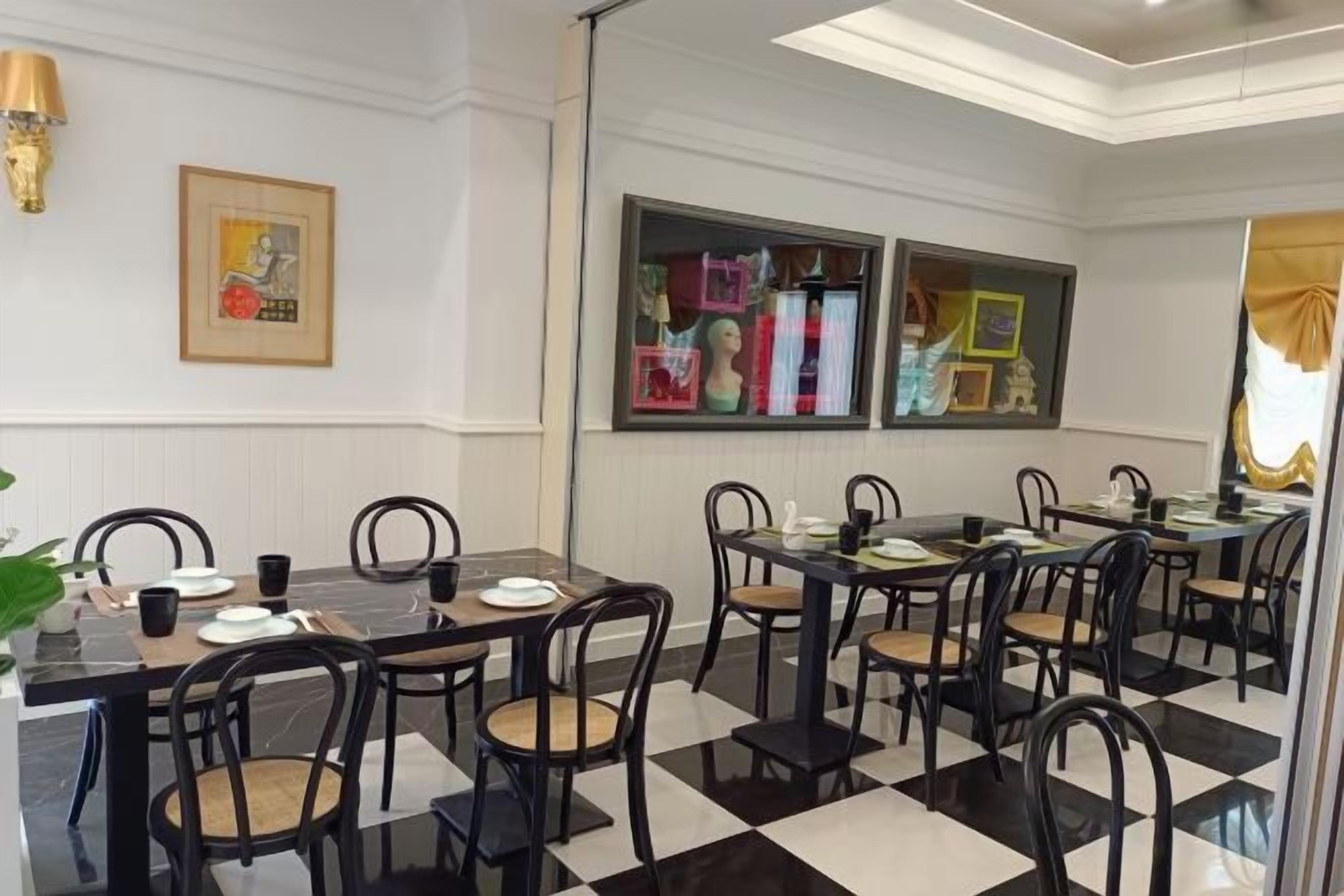 A hotel dining area with multiple tables and chairs, framed artwork on the walls, and a checkered floor pattern.