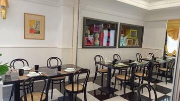 A hotel dining area with multiple tables and chairs, framed artwork on the walls, and a checkered floor pattern.