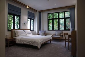 Een slaapkamer met een groot bed, twee stoelen, een nachtkastje en een raam met uitzicht op groen.