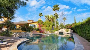 A swimming pool with a stone edge, surrounded by lush greenery and palm trees. - Keys Creek & Casita - Avantstay Sleeps 30 Estate Vineyard, Pool, Courts, Theater, Views (Valley Center)