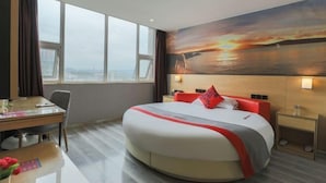 A hotel room with a large bed, a desk, and a view of a sunset over water. - Kaili New Century Hotel (Grand Cross of International Trade Shopping Center) (Kaili)
