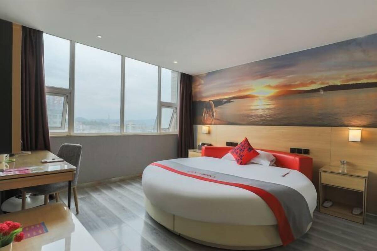 Habitación de hotel con una cama grande, un escritorio y vistas a un atardecer sobre el agua.