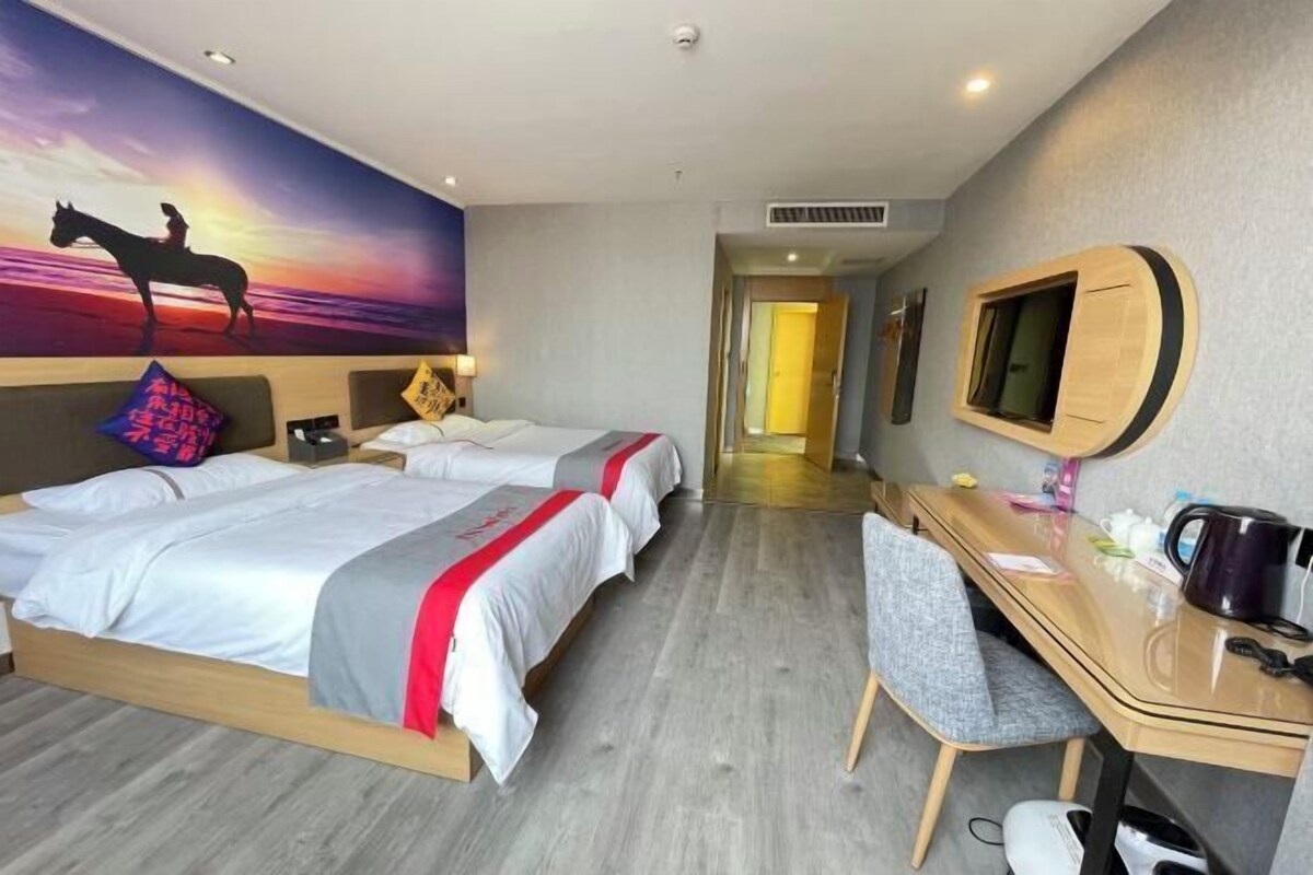 A hotel room with two beds, a desk, a chair, a TV, and a mural of a horse on a sunset.