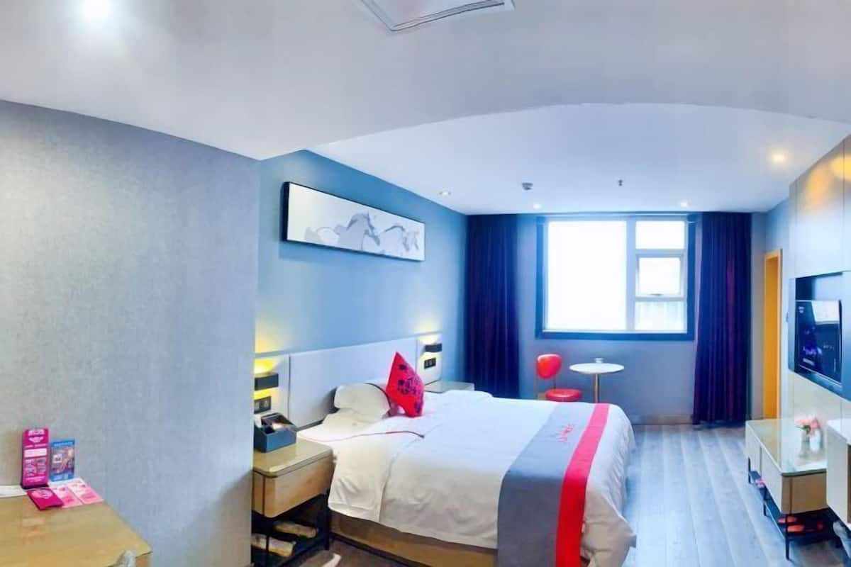 Habitación de hotel con cama, mesita de noche, lámpara, televisor y ventana con cortinas.