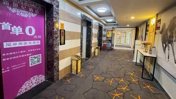 A hotel corridor with a patterned floor, a reception desk, and a wall with a QR code.