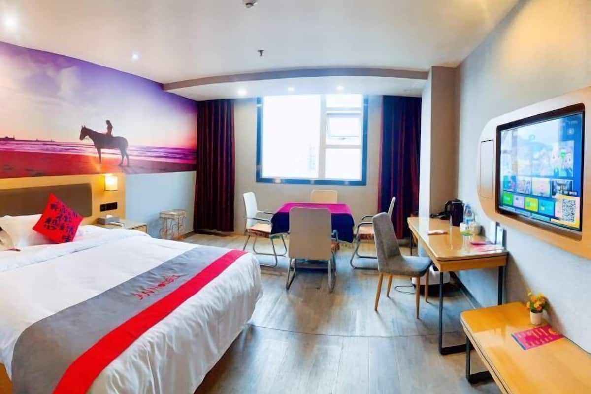 Una habitación de hotel con cama, escritorio, sillas, televisor y un mural.