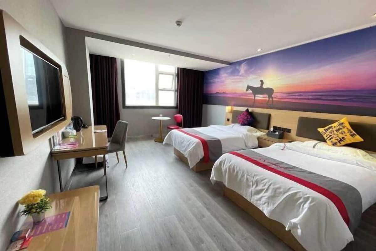 Habitación de hotel con dos camas, un escritorio, una silla, un televisor y un cuadro de un atardecer.