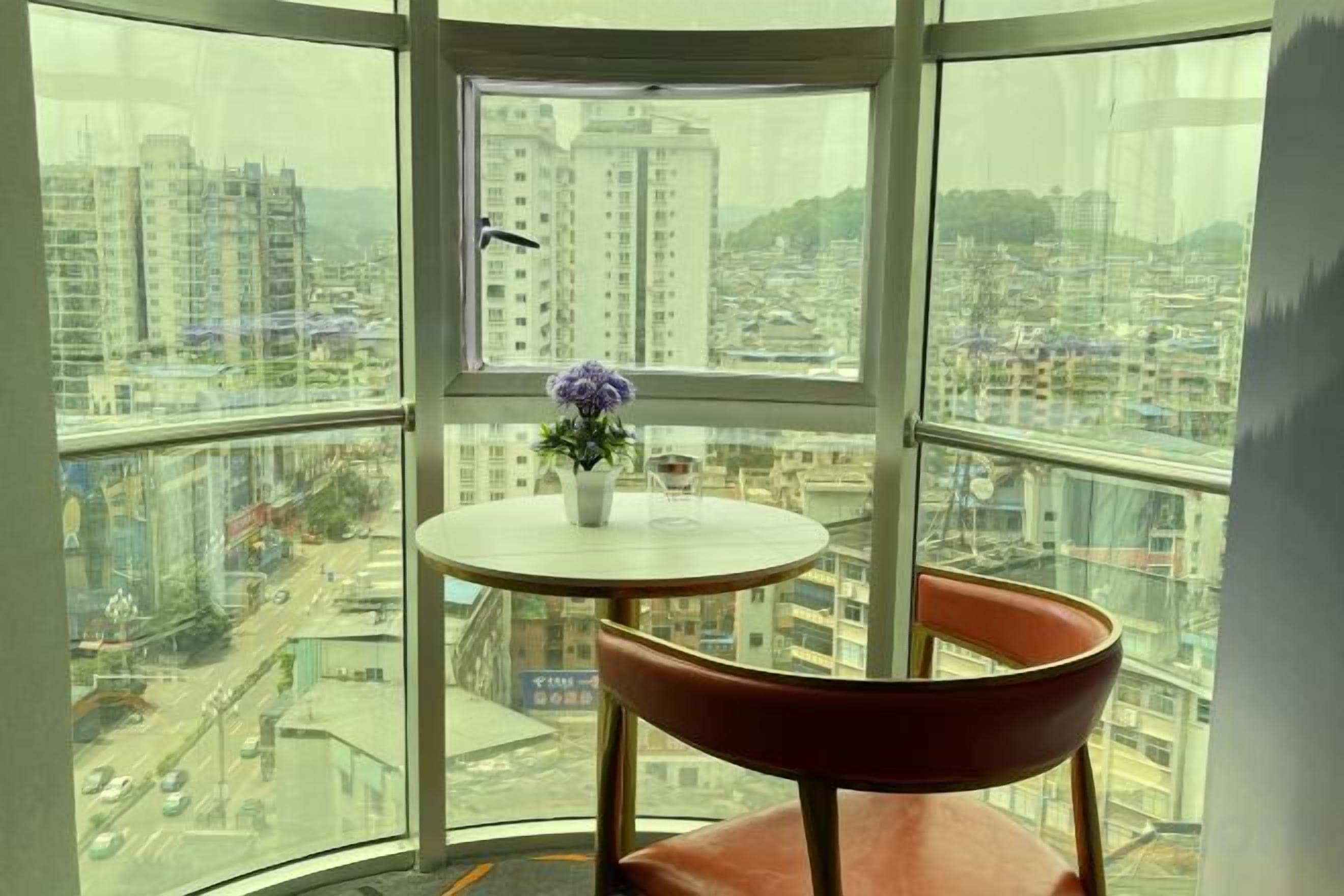 A room with a curved glass wall, a round table with a vase of flowers, and a single chair.
