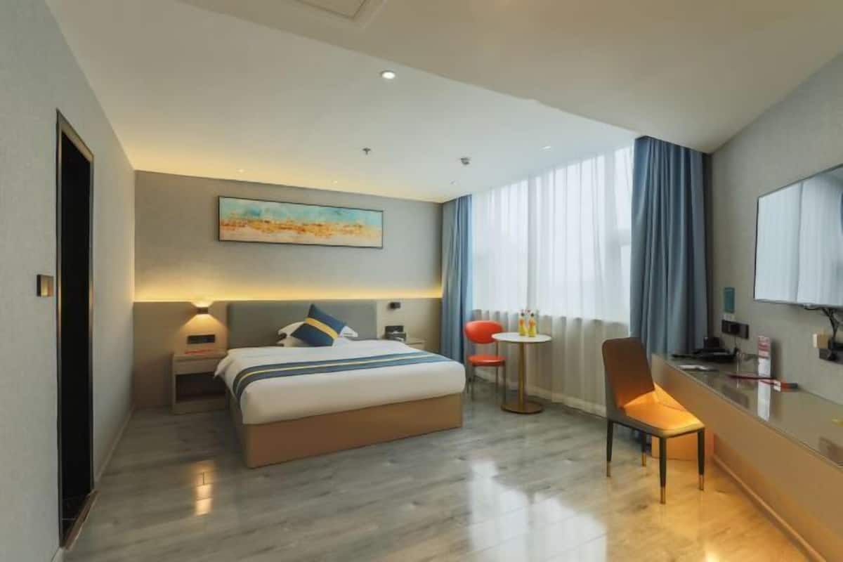 Una habitación de hotel moderna con cama, mesita de noche, silla y escritorio con ordenador.