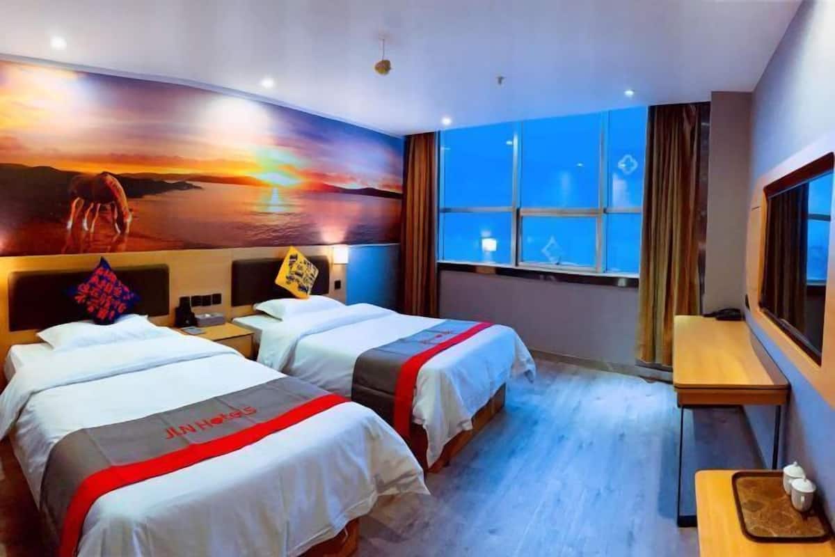 Habitación de hotel con dos camas, un mural grande en la pared, una ventana con cortinas y una mesita con bandeja.