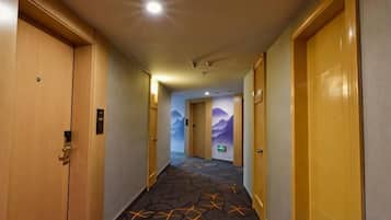 A hotel hallway with doors on both sides, carpeted floor, and a wall mural.