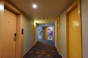 Un couloir d’hôtel avec des portes des deux côtés, un sol recouvert de moquette et une fresque murale.