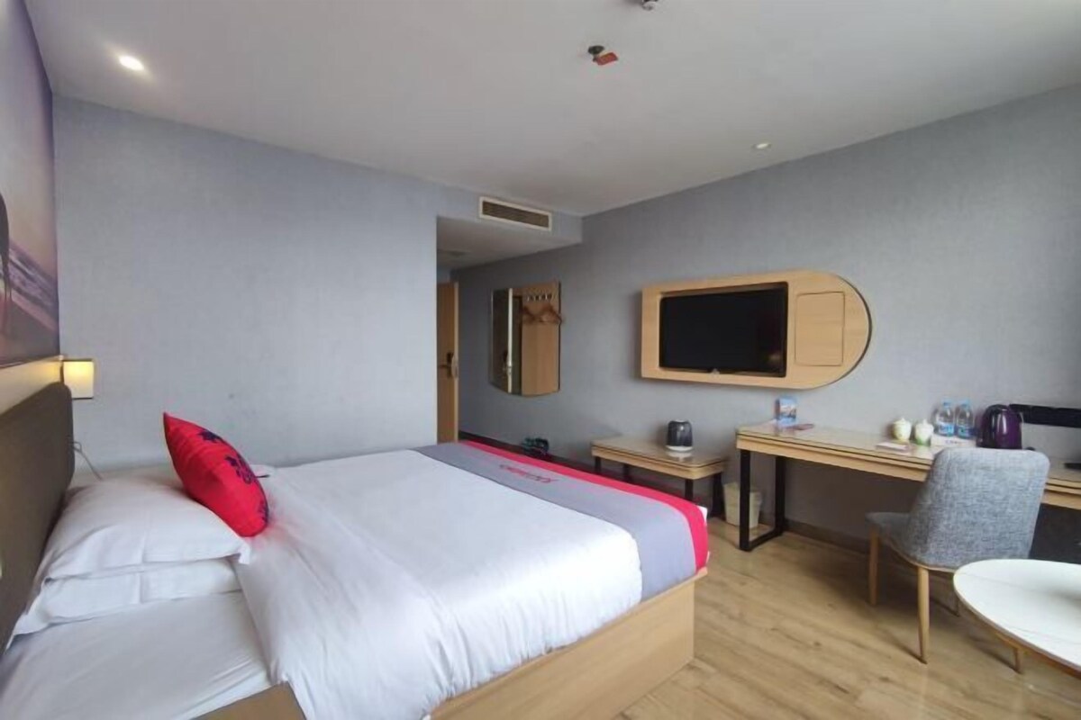 A hotel room with a bed, a desk, a chair, a television, and a mirror.