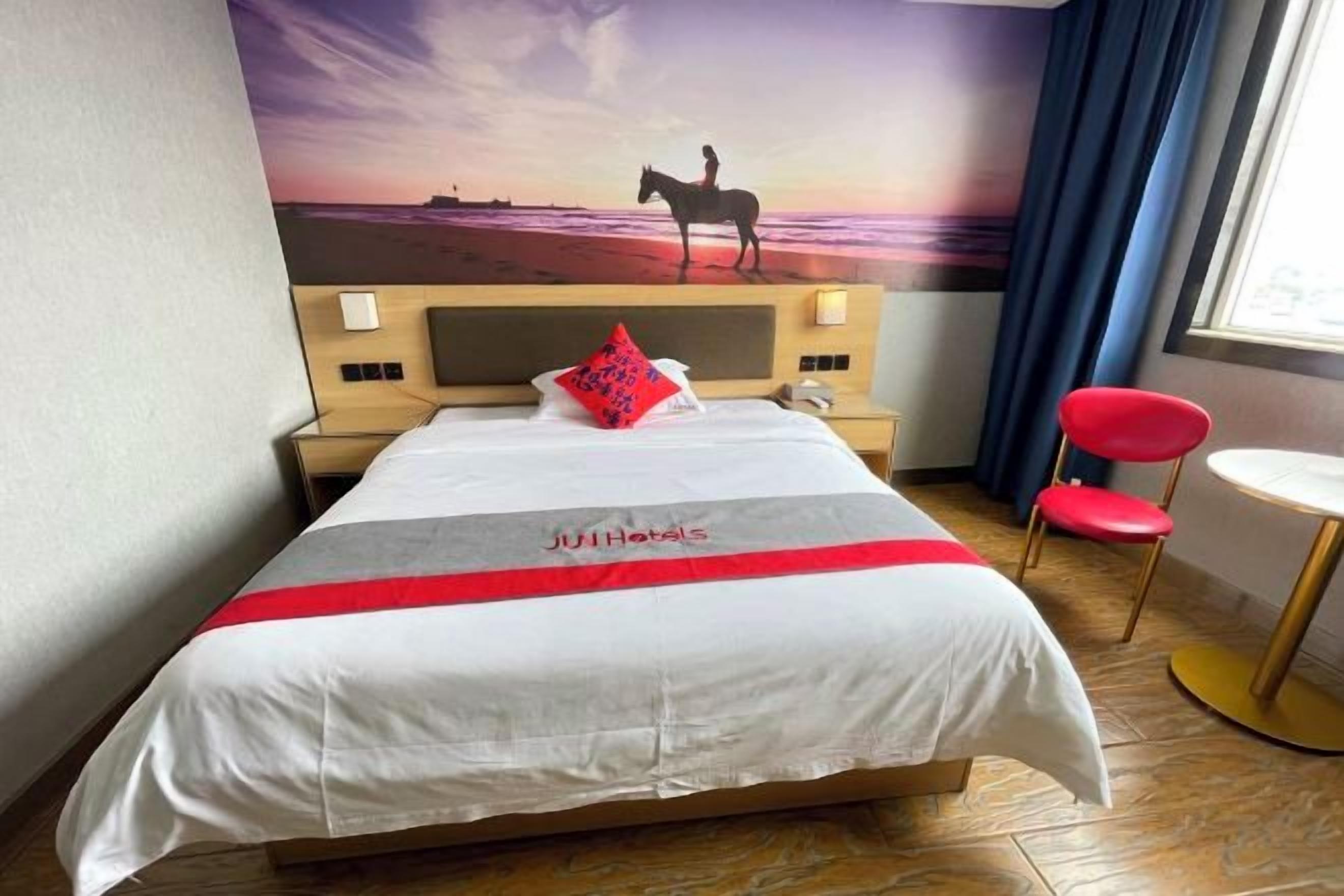 Une chambre d’hôtel avec un lit, une table de chevet, un fauteuil rouge et une fresque murale.
