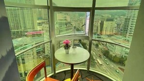 A corner room with a curved glass wall, a small table with a vase of flowers, and a chair. - Kaili New Century Hotel (Grand Cross of International Trade Shopping Center) (Kaili)