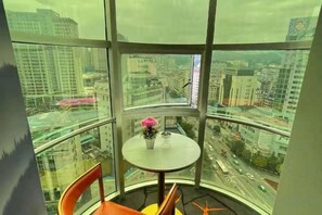 A room with a curved glass wall, a small round table with a flower, and two orange chairs. - Kaili New Century Hotel (Grand Cross of International Trade Shopping Center) (Kaili)