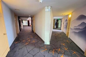 A hotel hallway with a geometric patterned floor, a light-colored pillar, and a mural on the right wall. - Kaili New Century Hotel (Grand Cross of International Trade Shopping Center) (Kaili)