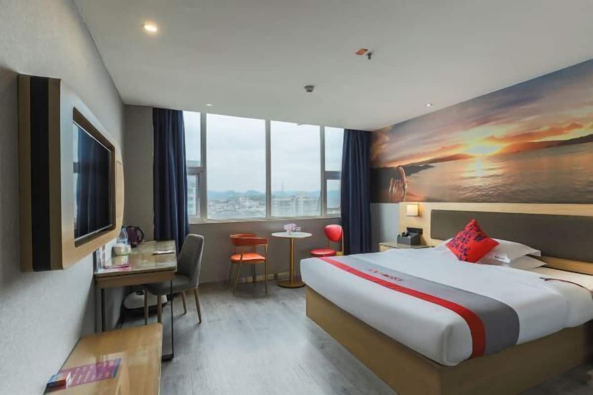 Habitación de hotel con una cama grande, un escritorio, dos sillas, una mesita y un cuadro de un atardecer en la pared.