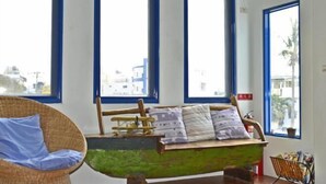 Et værelse med en grøn sovesofa, en fletstol og store vinduer med blå rammer.