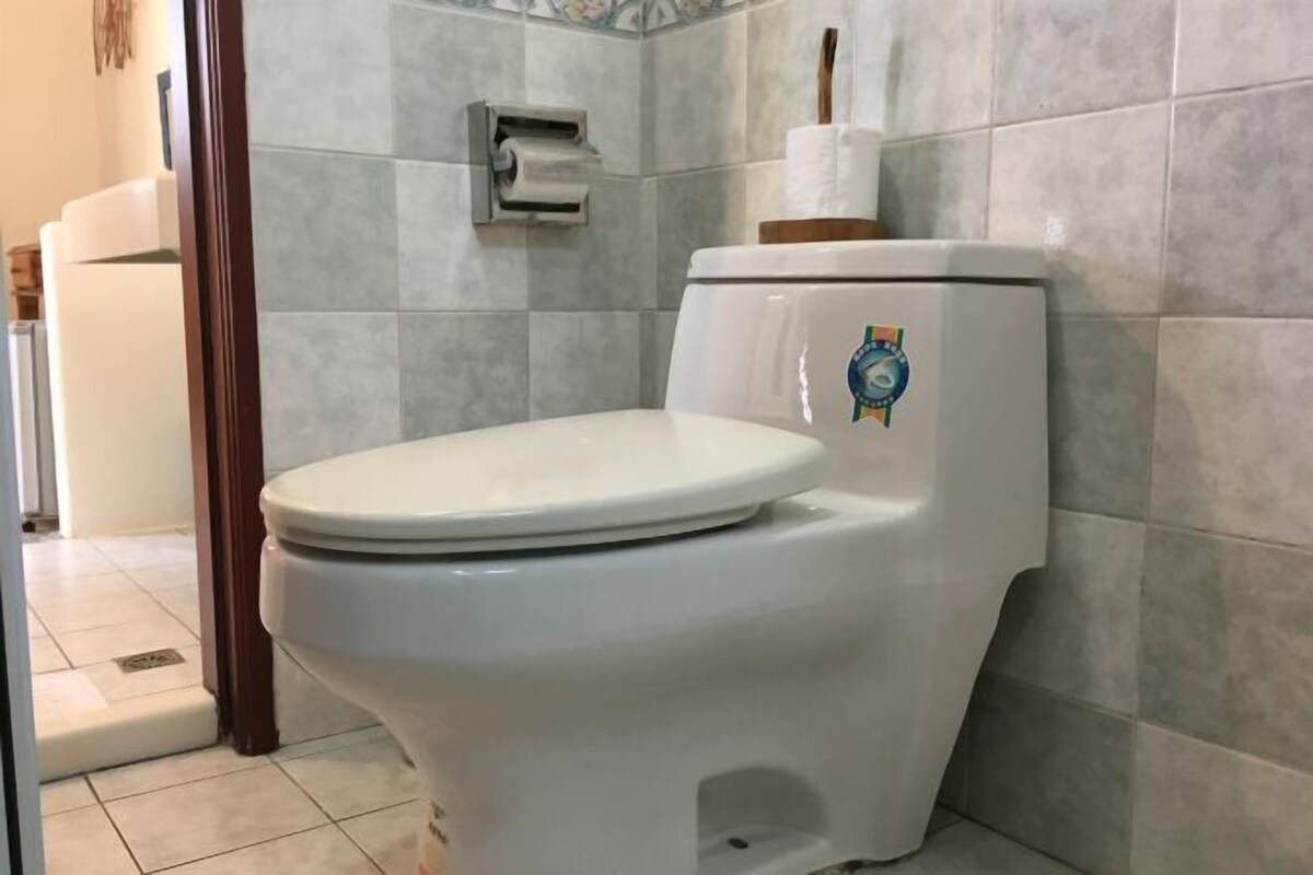 A toilet with a white seat and lid, a toilet paper holder on the wall, and a tiled floor.