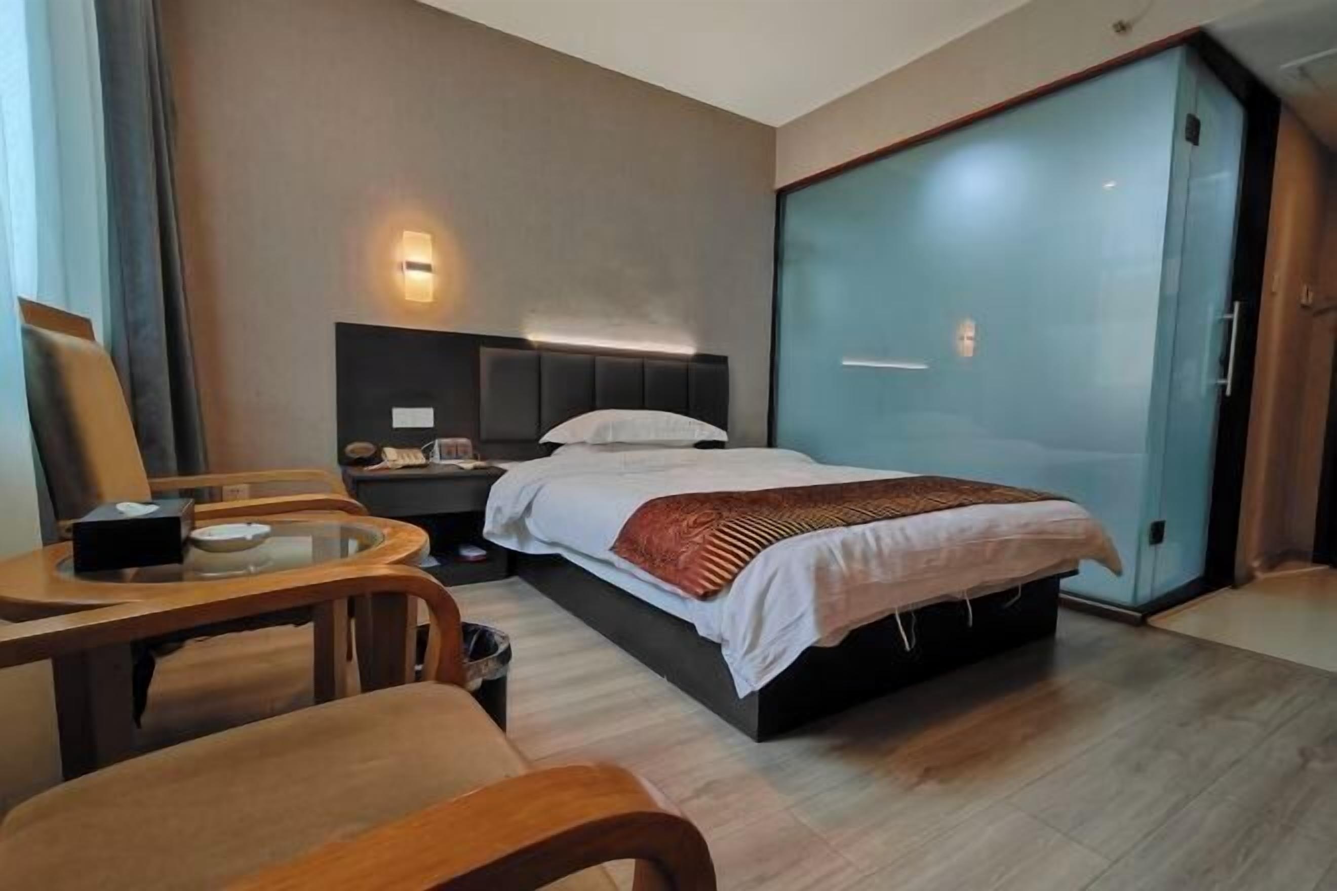 A modern hotel room with a large bed, a desk, and a glass partition.