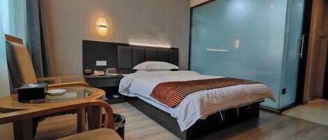 A modern hotel room with a large bed, a desk, and a glass partition.