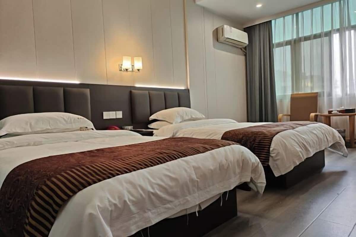 A hotel room with two beds, a nightstand, a lamp, and a window with curtains.
