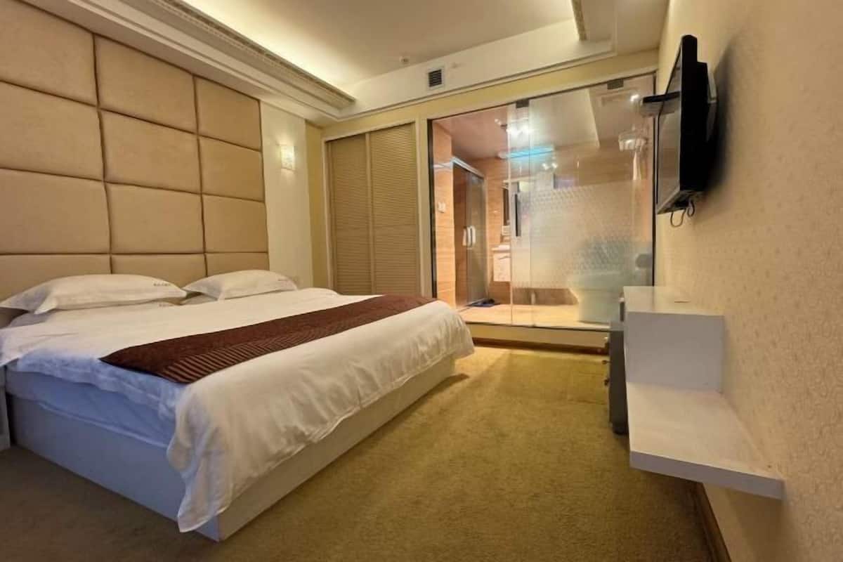 A hotel room with a bed, a bedside table, a TV mounted on the wall, and a sliding door leading to a bathroom.