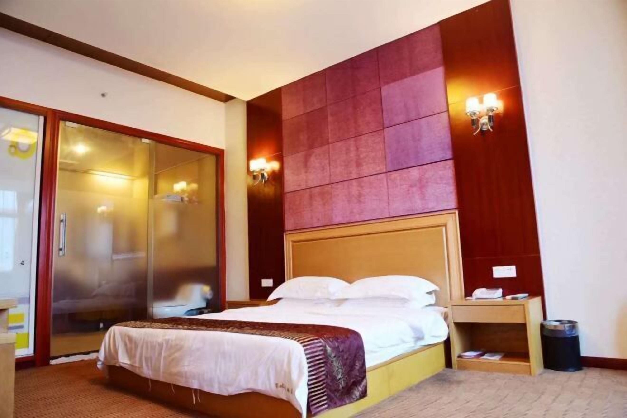 A hotel room with a bed, a wooden headboard, a nightstand, a trash bin, and a sliding door closet.