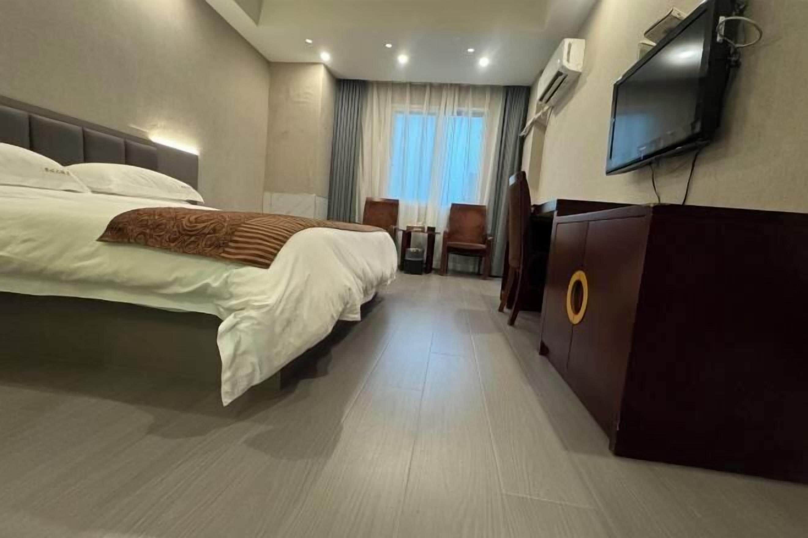 A hotel room with a large bed, a desk with a chair, a television, and a minibar.