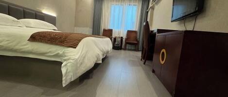 A hotel room with a large bed, a desk with a chair, a television, and a minibar.