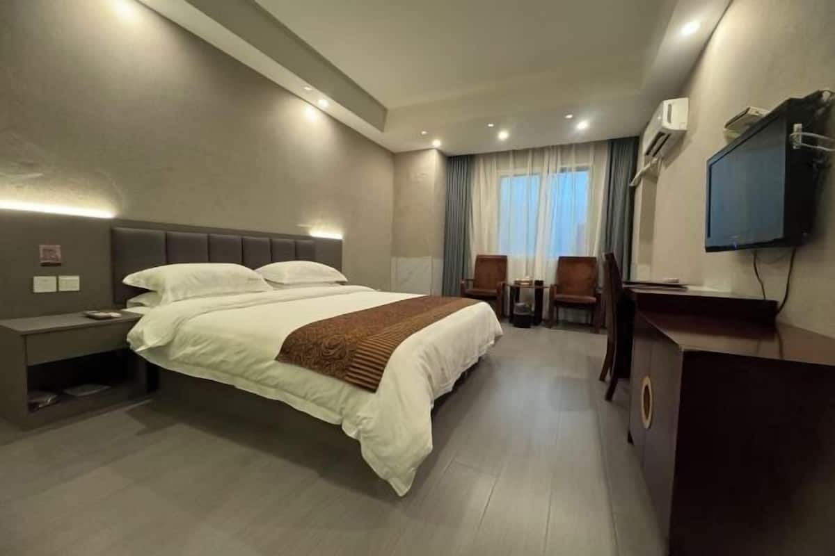 A modern hotel room with a large bed, bedside tables, a desk, a chair, and a TV mounted on the wall.