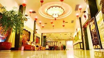 A hotel lobby with a chandelier, red lanterns, a reception desk, and seating areas.