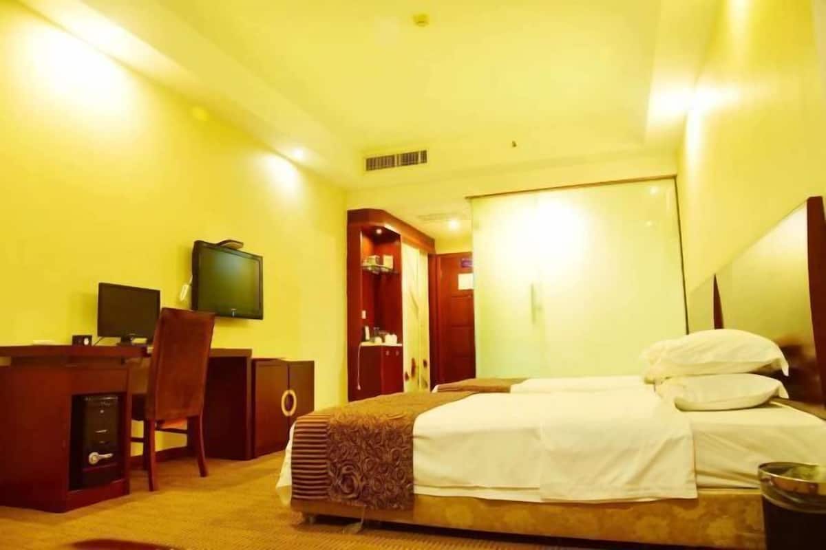 A hotel room with a bed, desk, chair, television, and a door leading to another room.