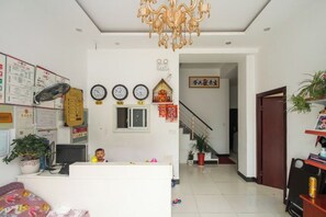A reception area with a desk, chairs, a chandelier, clocks, and a staircase leading to another room. - Xinghua Xiangyun Hotel (Xinghua)