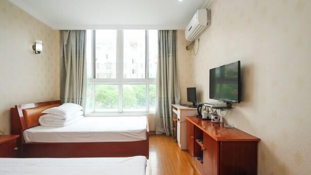 A hotel room with two beds, a desk with a TV, and a window with curtains.