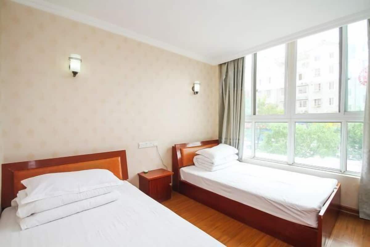 A hotel room with two beds, a nightstand, and a window with curtains.