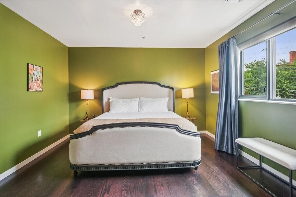 Una camera da letto con un letto grande, due lampade da comodino, una panca e una finestra con tende.