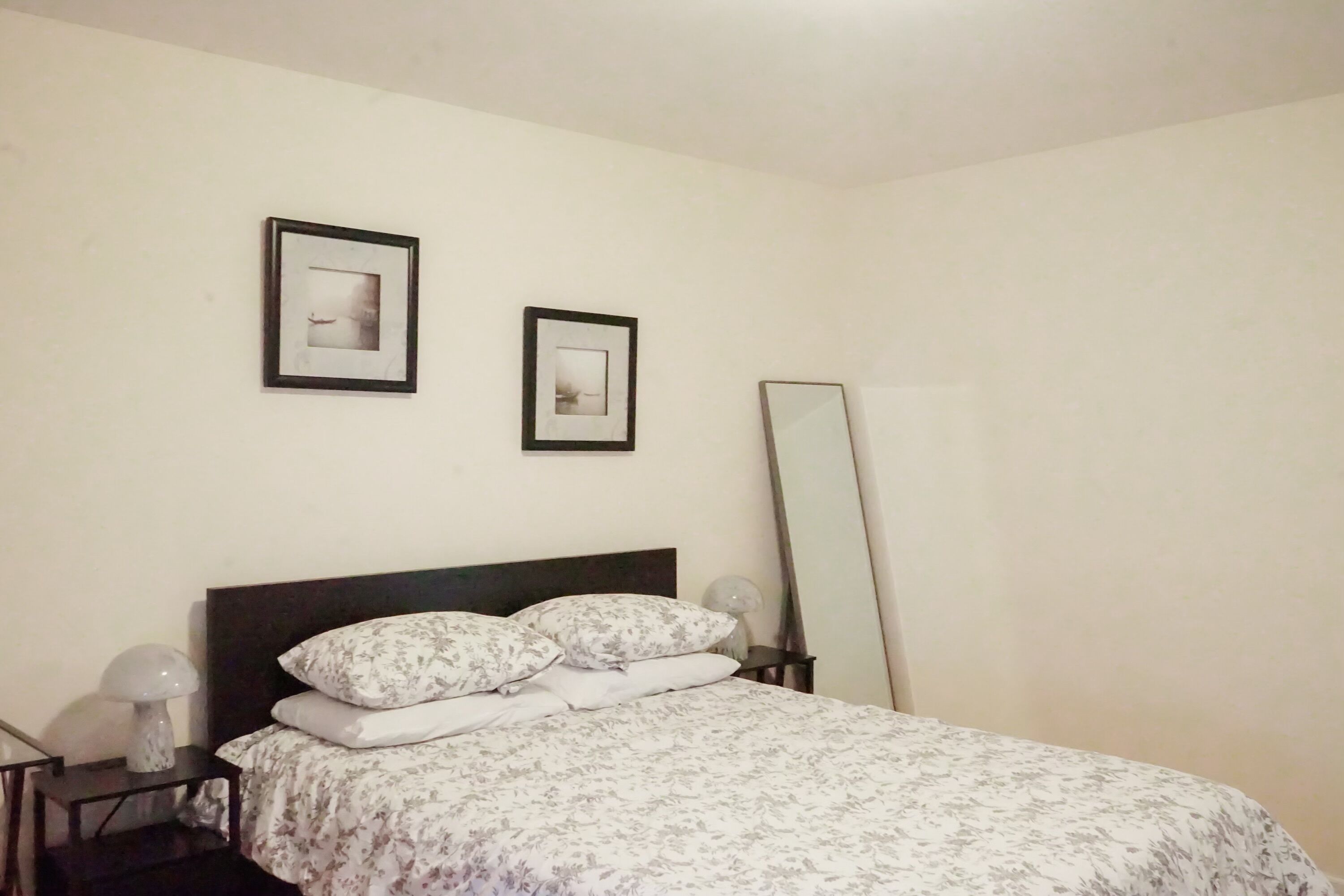 A neatly made bed with floral bedding, a bedside table with a lamp, and two framed pictures on the wall.