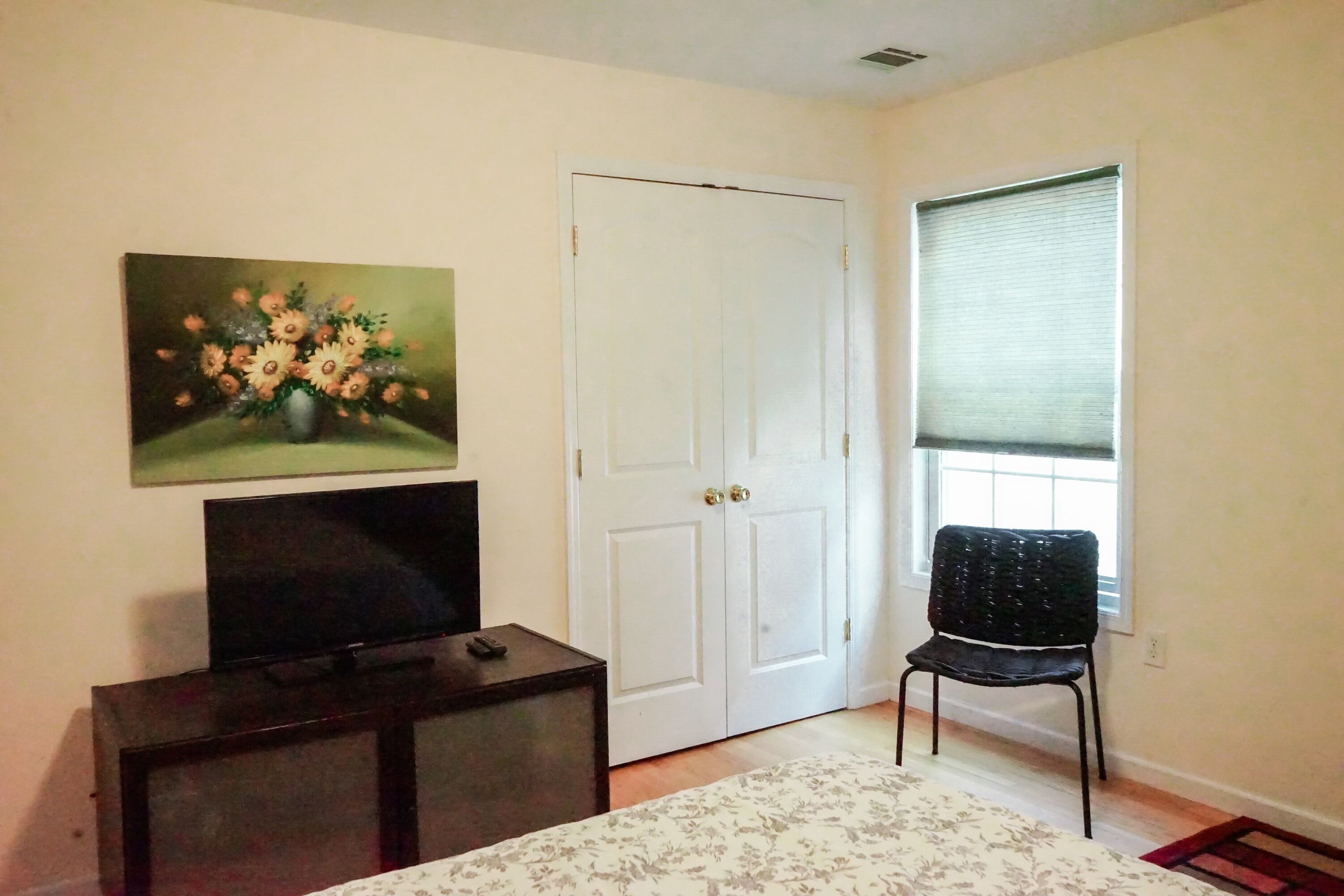 A bedroom with a bed, a dresser, a television, a painting, a door, and a window.