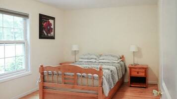 A bedroom with a wooden bed, two bedside tables with lamps, a window, and a framed picture on the wall.