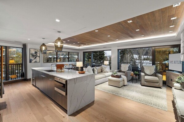 A modern kitchen with a marble island, a dining area with a sofa and chairs, and a living room with a TV and seating.