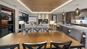 Una cocina moderna con una isla central, una zona de comedor con mesa de madera y un espacio de sala de estar con chimenea.