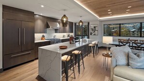 Una cocina moderna con armarios oscuros, una isla de mármol y taburetes de bar.