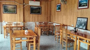 A dining area with wooden tables and chairs, framed pictures on the walls, and an air conditioning unit.