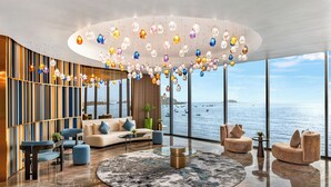 Un intérieur moderne avec un espace salon circulaire, de grandes fenêtres offrant une vue sur la mer et des luminaires décoratifs suspendus.